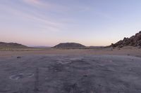 a large rock sitting on top of a field near a dry landscape under a pink sky
