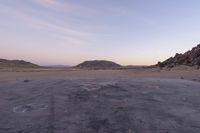 a large rock sitting on top of a field near a dry landscape under a pink sky
