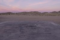 a large rock sitting on top of a field near a dry landscape under a pink sky