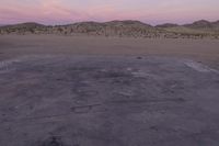 a large rock sitting on top of a field near a dry landscape under a pink sky