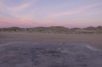 a large rock sitting on top of a field near a dry landscape under a pink sky