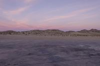 a large rock sitting on top of a field near a dry landscape under a pink sky