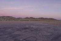 a large rock sitting on top of a field near a dry landscape under a pink sky
