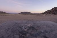 a large rock sitting on top of a field near a dry landscape under a pink sky