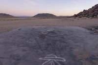 a large rock sitting on top of a field near a dry landscape under a pink sky