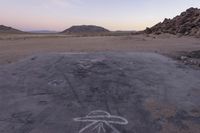 a large rock sitting on top of a field near a dry landscape under a pink sky