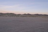 a large rock sitting on top of a field near a dry landscape under a pink sky