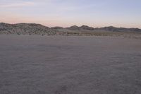 a large rock sitting on top of a field near a dry landscape under a pink sky