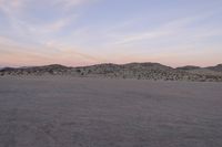 a large rock sitting on top of a field near a dry landscape under a pink sky
