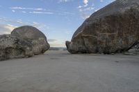 there are two large rocks on the ground in the desert between them is a rock and some blue sky
