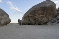 there are two large rocks on the ground in the desert between them is a rock and some blue sky