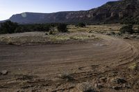 a dirt field and a dry landscape with trees in the middle of it and hills in the background