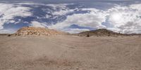 a very wide angle view of some desert landscape with clouds above it and in the background,