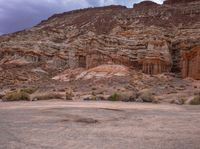 this horse stands in the desert with its back legs crossed and feet up, with rocky landscape behind him