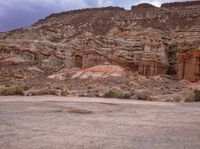 this horse stands in the desert with its back legs crossed and feet up, with rocky landscape behind him