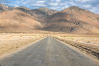 a large open country road in the desert with mountains behind it and a cloud filled sky above