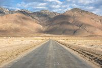 a large open country road in the desert with mountains behind it and a cloud filled sky above