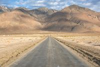 a large open country road in the desert with mountains behind it and a cloud filled sky above