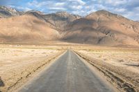 a large open country road in the desert with mountains behind it and a cloud filled sky above