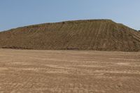 a lone bench sits in a open desert field, with a large hill in the background