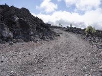 a barren road that is made of gravel and rocks with some clouds in the background