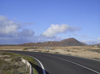 a large wide highway that is on a hill side with a few mountains and clouds in the distance