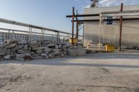 large pile of stones sitting next to building under construction crane and equipment with blue sky in the background