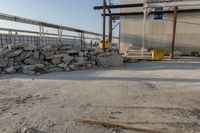 large pile of stones sitting next to building under construction crane and equipment with blue sky in the background