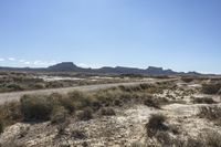 an empty road in a wide open plain of land near mountains and water on a sunny day