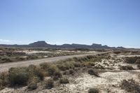 an empty road in a wide open plain of land near mountains and water on a sunny day