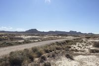 an empty road in a wide open plain of land near mountains and water on a sunny day