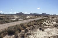 an empty road in a wide open plain of land near mountains and water on a sunny day