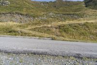 a person riding a skateboard down a steep hill next to a dirt road with mountains