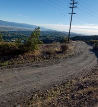 the dirt road with telephone lines in front of it on top of a hill near the mountains