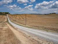 the dirt road runs alongside the fenced off farm land and has a small hill in the distance