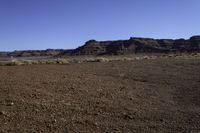 a dirt covered field near rocks and some mountains on a sunny day in the desert