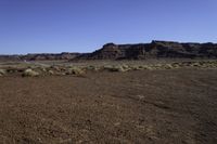 a dirt covered field near rocks and some mountains on a sunny day in the desert