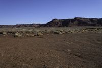 a dirt covered field near rocks and some mountains on a sunny day in the desert