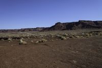 a dirt covered field near rocks and some mountains on a sunny day in the desert