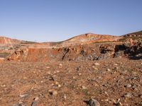 an empty dirt field in the middle of nowhere surrounded by hills and rocks in the background