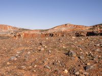 an empty dirt field in the middle of nowhere surrounded by hills and rocks in the background