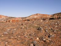 an empty dirt field in the middle of nowhere surrounded by hills and rocks in the background