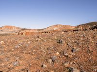 an empty dirt field in the middle of nowhere surrounded by hills and rocks in the background