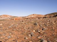 an empty dirt field in the middle of nowhere surrounded by hills and rocks in the background