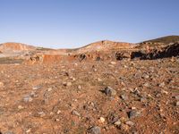 an empty dirt field in the middle of nowhere surrounded by hills and rocks in the background