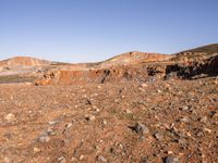 an empty dirt field in the middle of nowhere surrounded by hills and rocks in the background