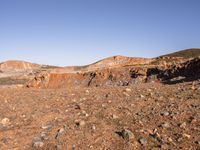 an empty dirt field in the middle of nowhere surrounded by hills and rocks in the background