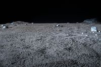 an image of desert at night, with rocks scattered on the ground and a light shines in the sky