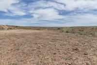 a dirt and rock field next to a desert area, with a large field and dirt path in the distance