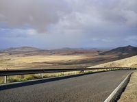 a road with an empty section below the mountain and clouds overhead above it in the distance,